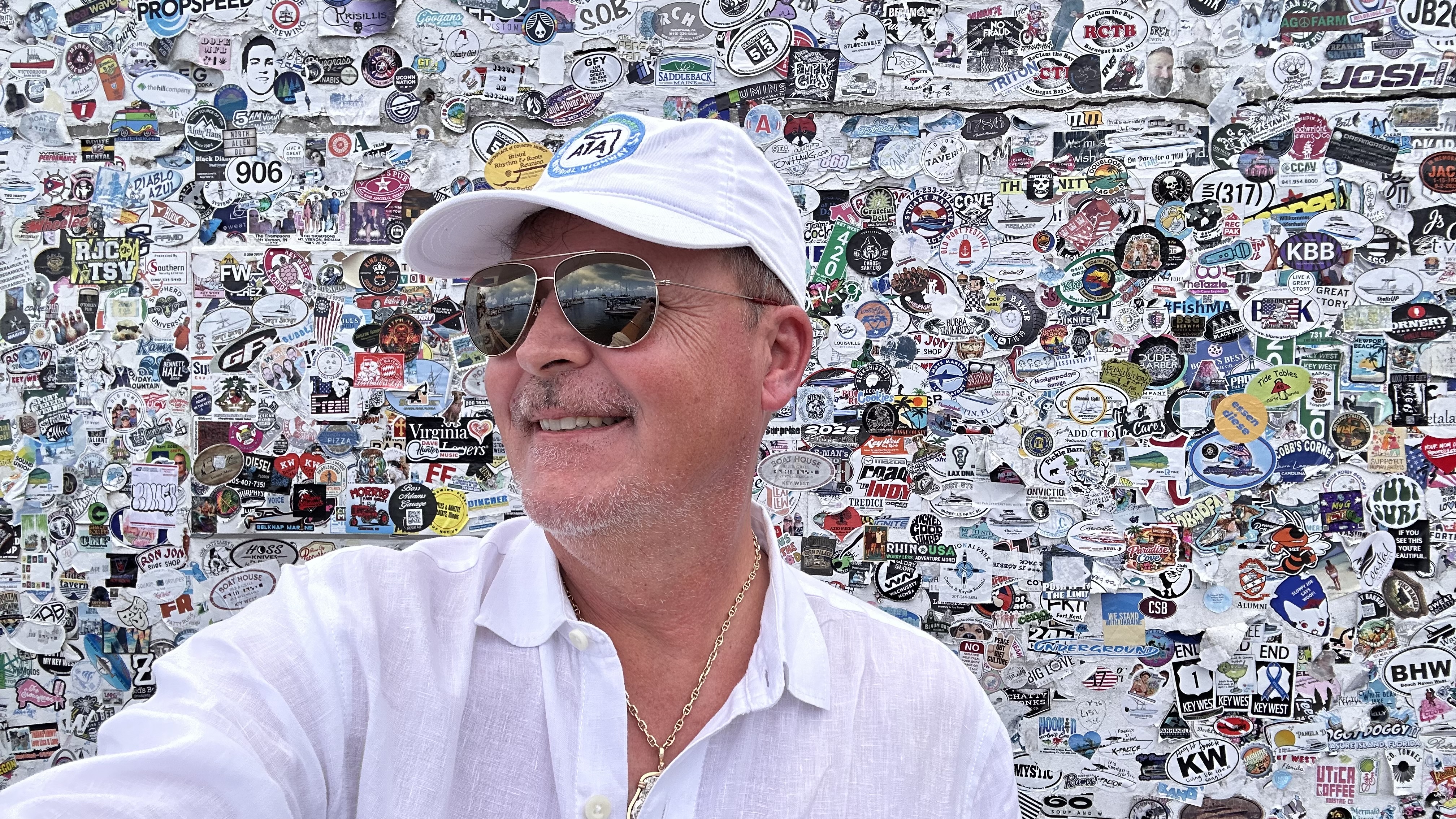 Bo Calloway in a white cap and sunglasses in front of a sticker-covered wall.